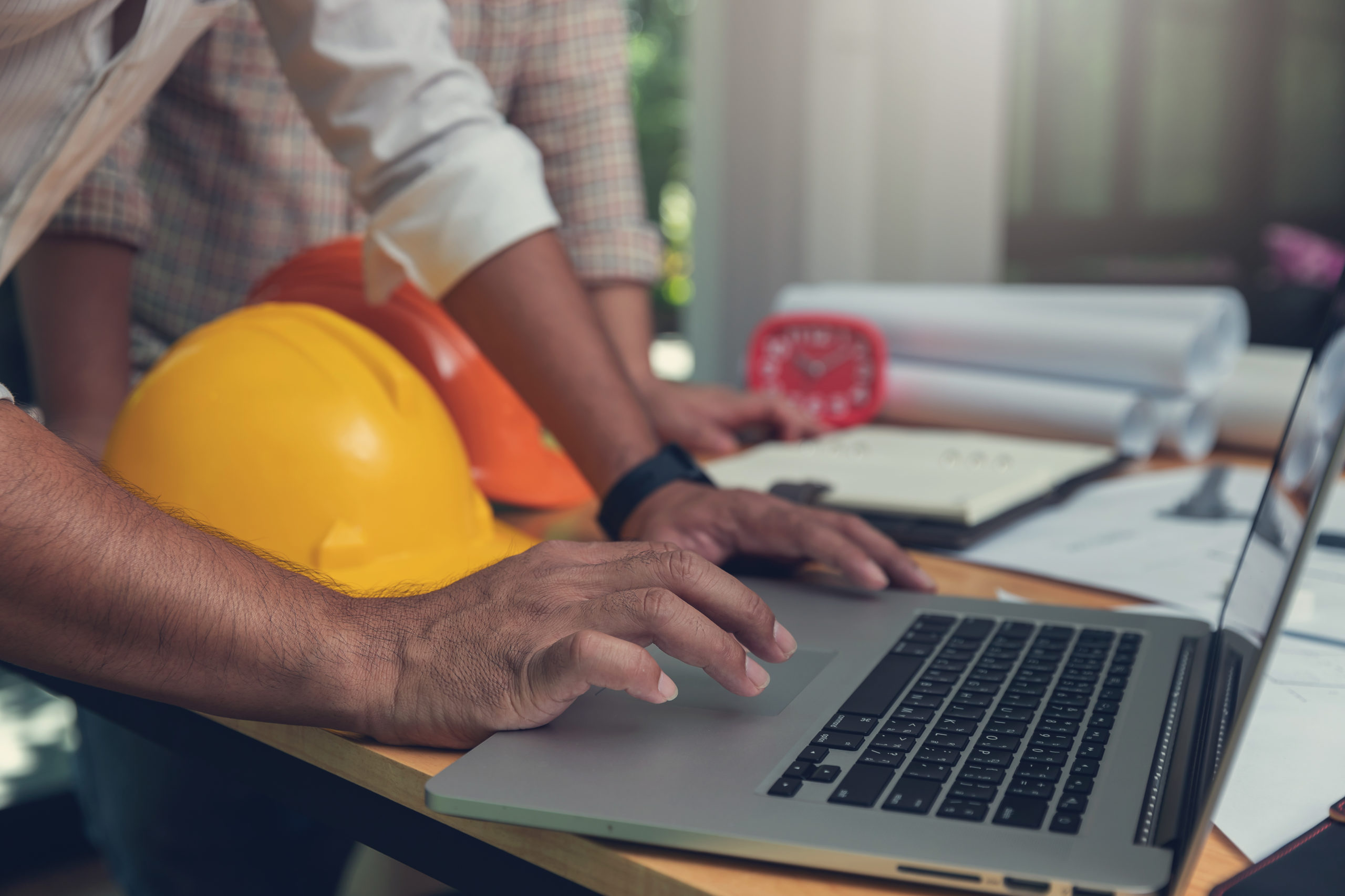 Person leading on table with laptop and yellow construction helmet