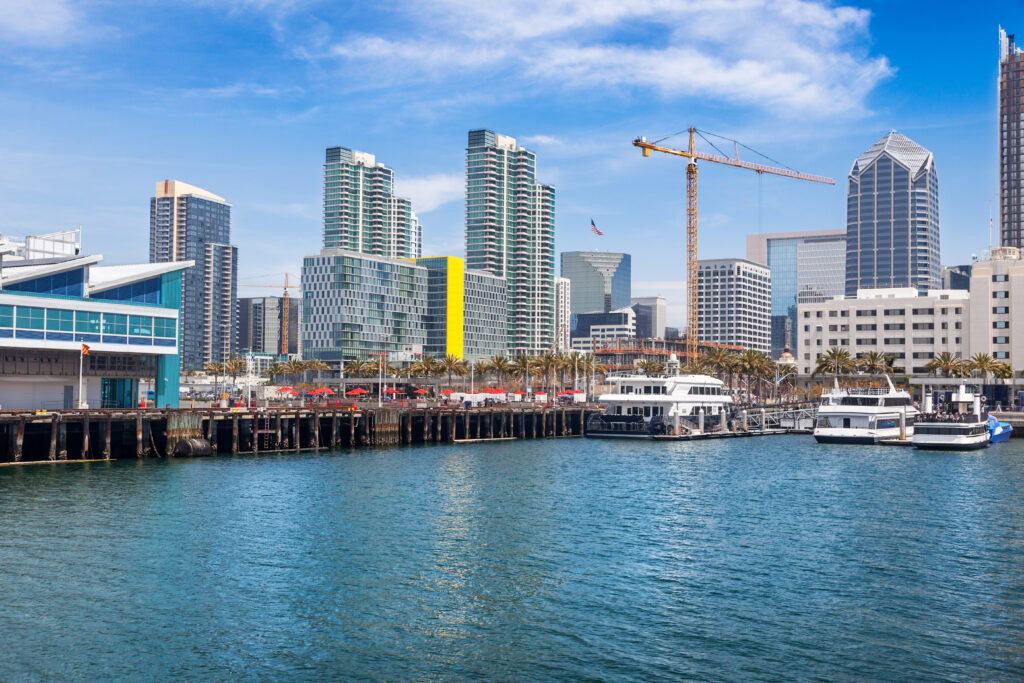 San Diego skyline with harbor and boats, clear blue sky, construction crane in view.