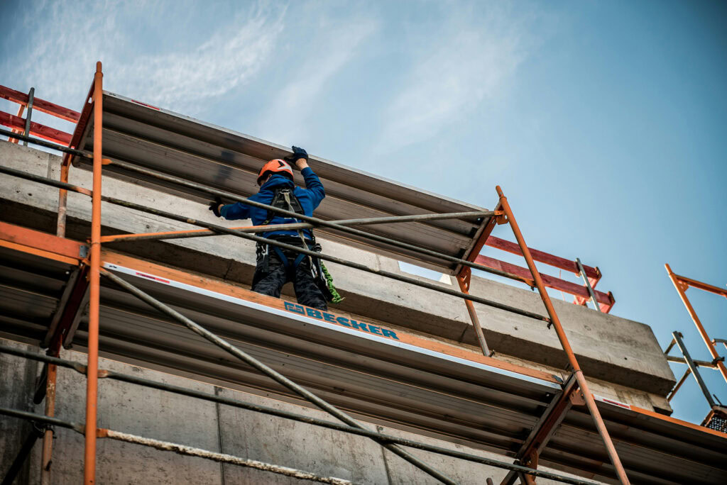 Worker in safety harness and hard hat on scaffolding at a construction site