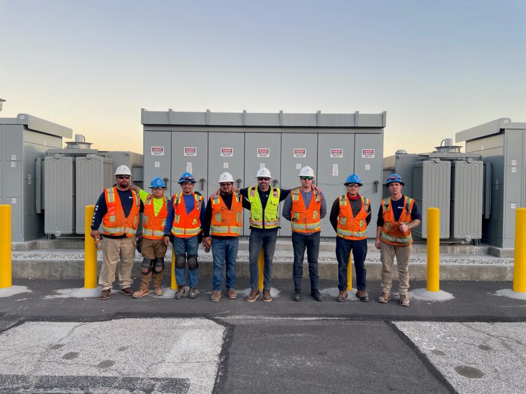 Group of construction workers in safety gear standing outside electrical equipment