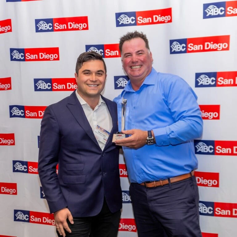 Two men posing with an award at a step-and-repeat banner