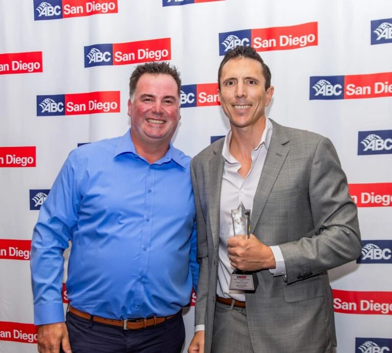 Two men smiling with an award at a step-and-repeat banner