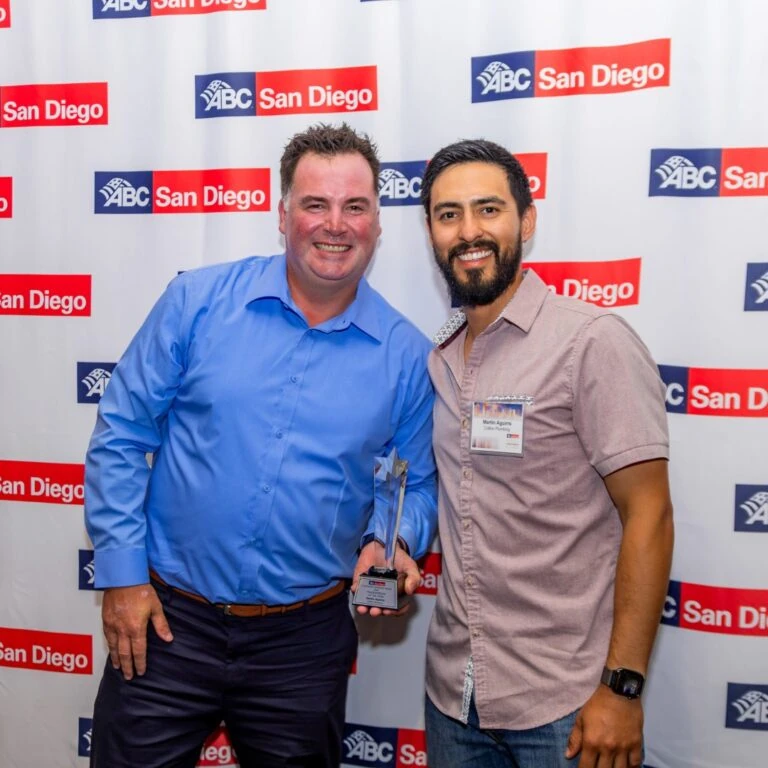 Two men smiling with an award at a step-and-repeat banner