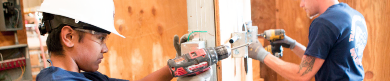 Two apprentices drilling into wood wall framing with cordless drills