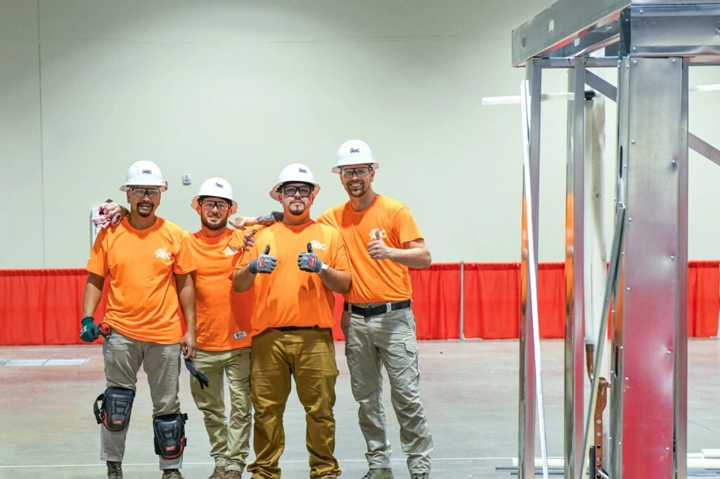 Four workers in orange ABC shirts and hard hats giving thumbs up at a craft competition