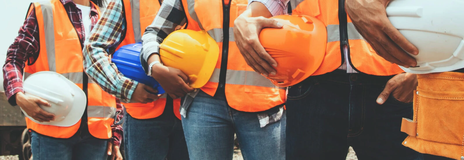 Row of construction workers in safety vests holding hard hats