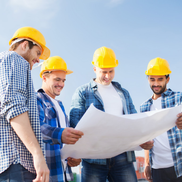 Four workers in hard hats reviewing blueprints outdoors
