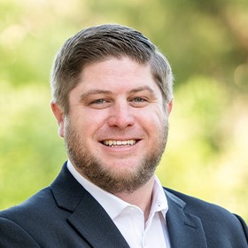 Professional headshot of a bearded man in a dark blazer