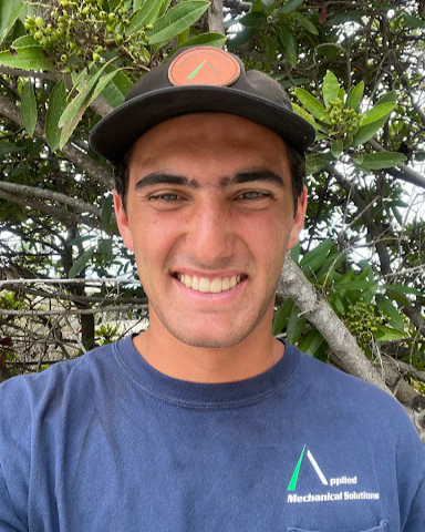 Professional headshot of a young man in a cap and blue shirt outdoors