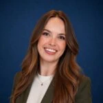 Portrait of Madison Picotte with long brown hair smiling against a blue background.