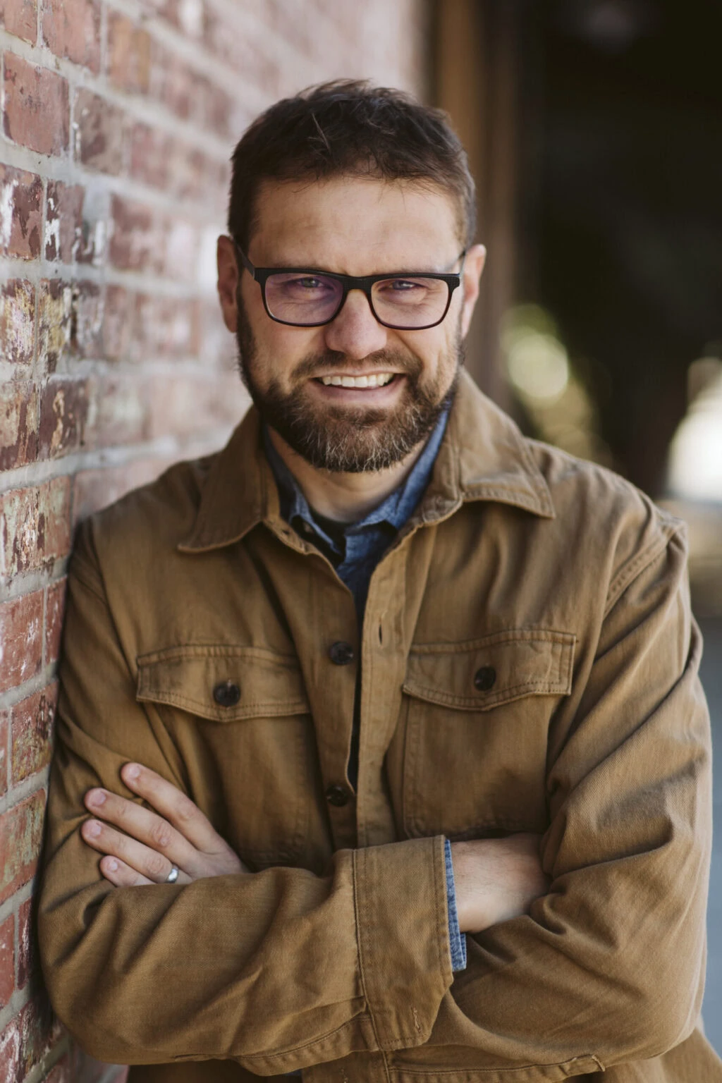 Professional headshot of a bearded man in a tan jacket