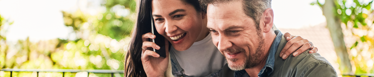 Smiling woman on a phone next to a man outdoors