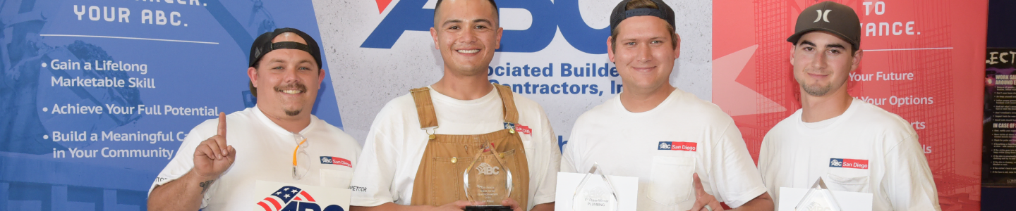 Four men holding awards at a construction event backdrop