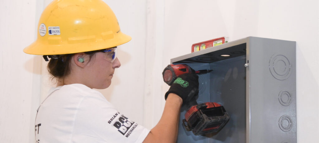 Woman in hard hat installing wiring in an electrical panel