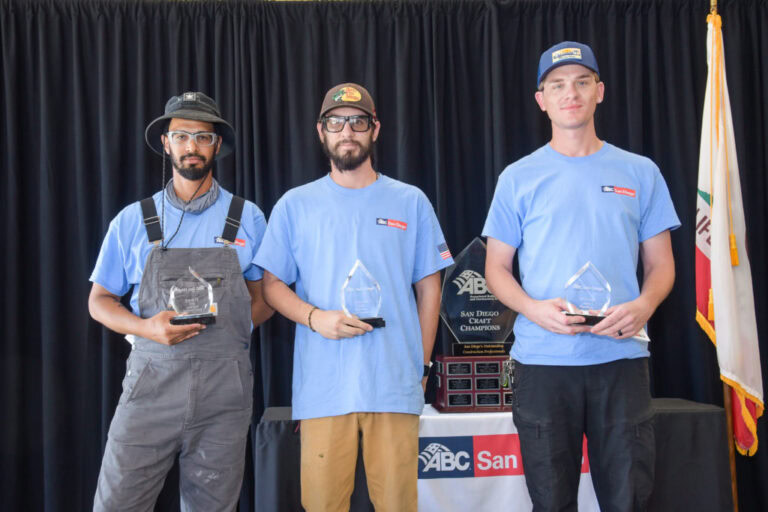 Three award winners holding trophies in front of a backdrop