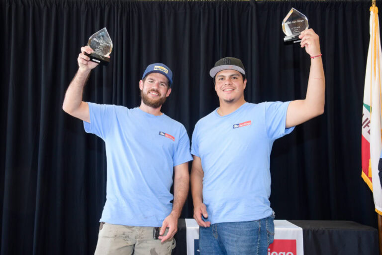 Two men holding up award trophies at a ceremony