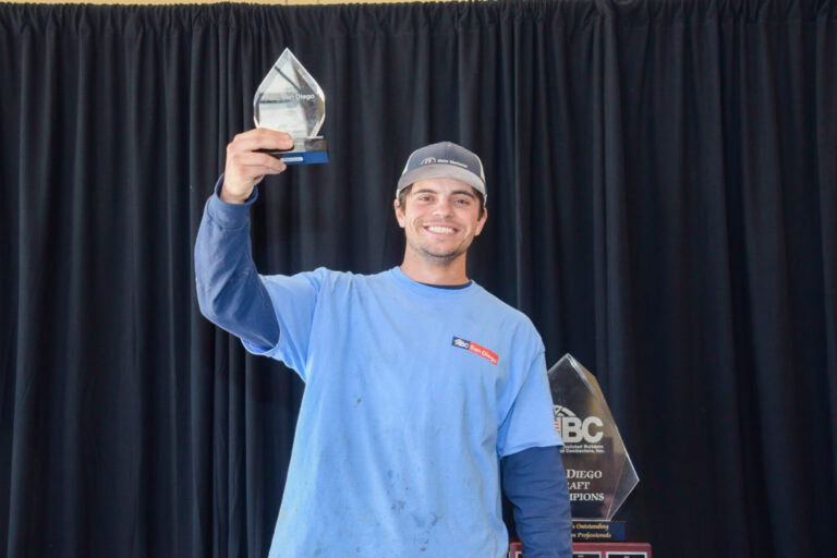 Man in a blue shirt holding up an award trophy