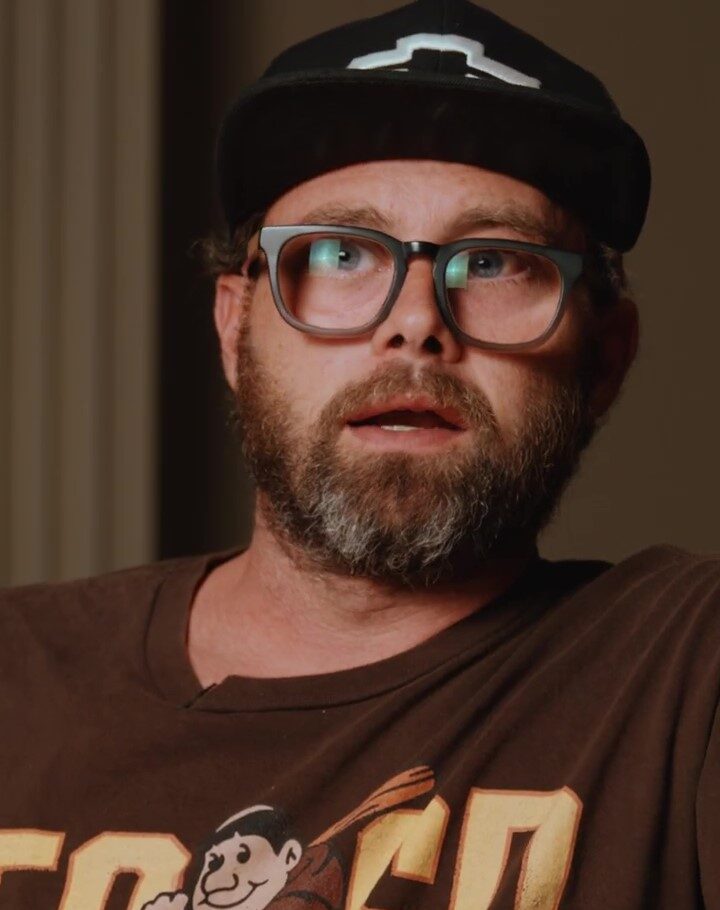 Headshot of a bearded man wearing glasses and a cap