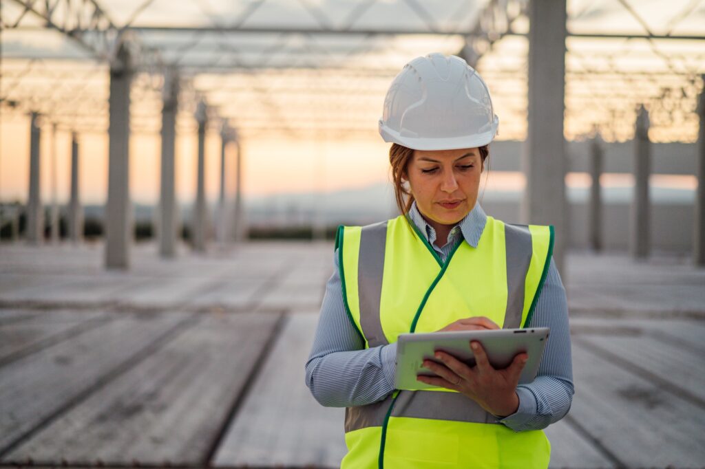 Woman in hard hat and safety vest using a tablet at a construction site