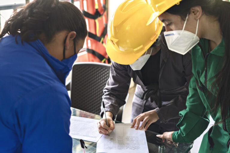 Workers in hard hats and face masks reviewing a document together