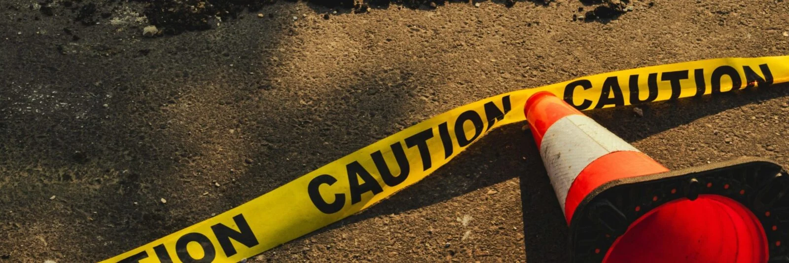 Yellow caution tape and an orange traffic cone on the ground