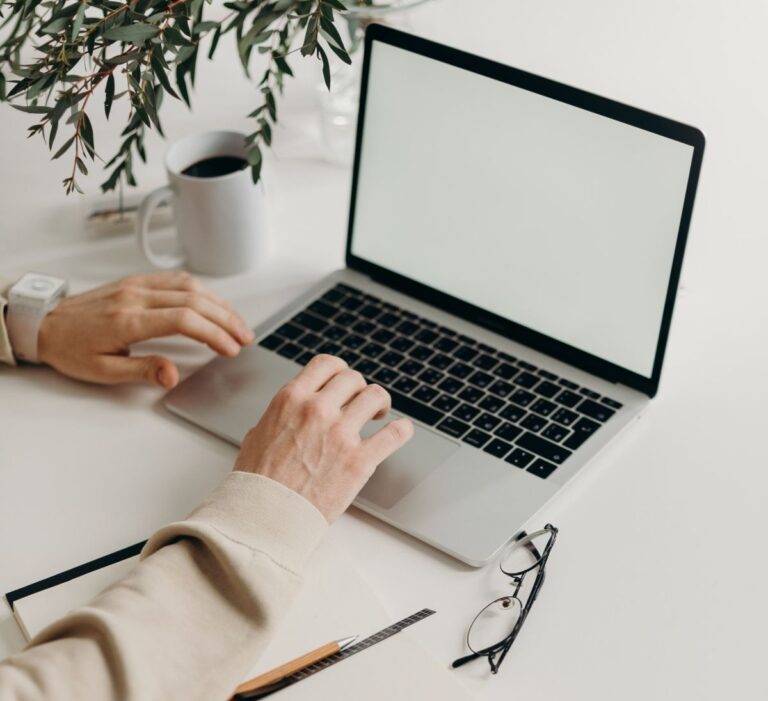 Person typing on a laptop at a desk with coffee and plant