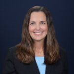 Professional woman with brown hair smiling, wearing a black blazer and blue top.