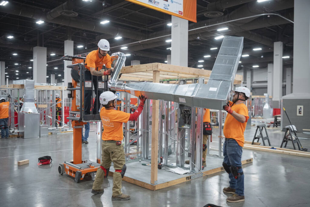 Construction workers assembling a model house at an indoor exhibition.