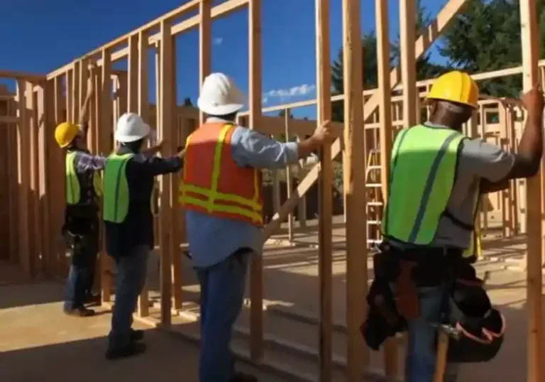 Construction workers in safety gear assembling a wooden building frame.